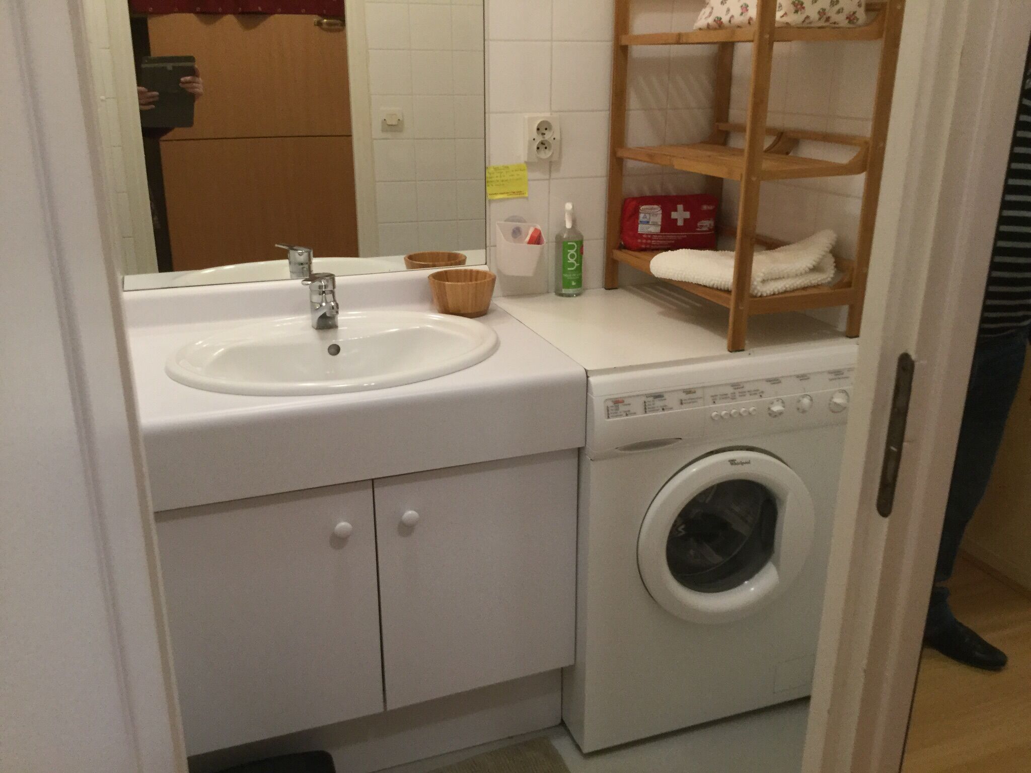 A compact bathroom with a sink, mirror, and a washing machine.