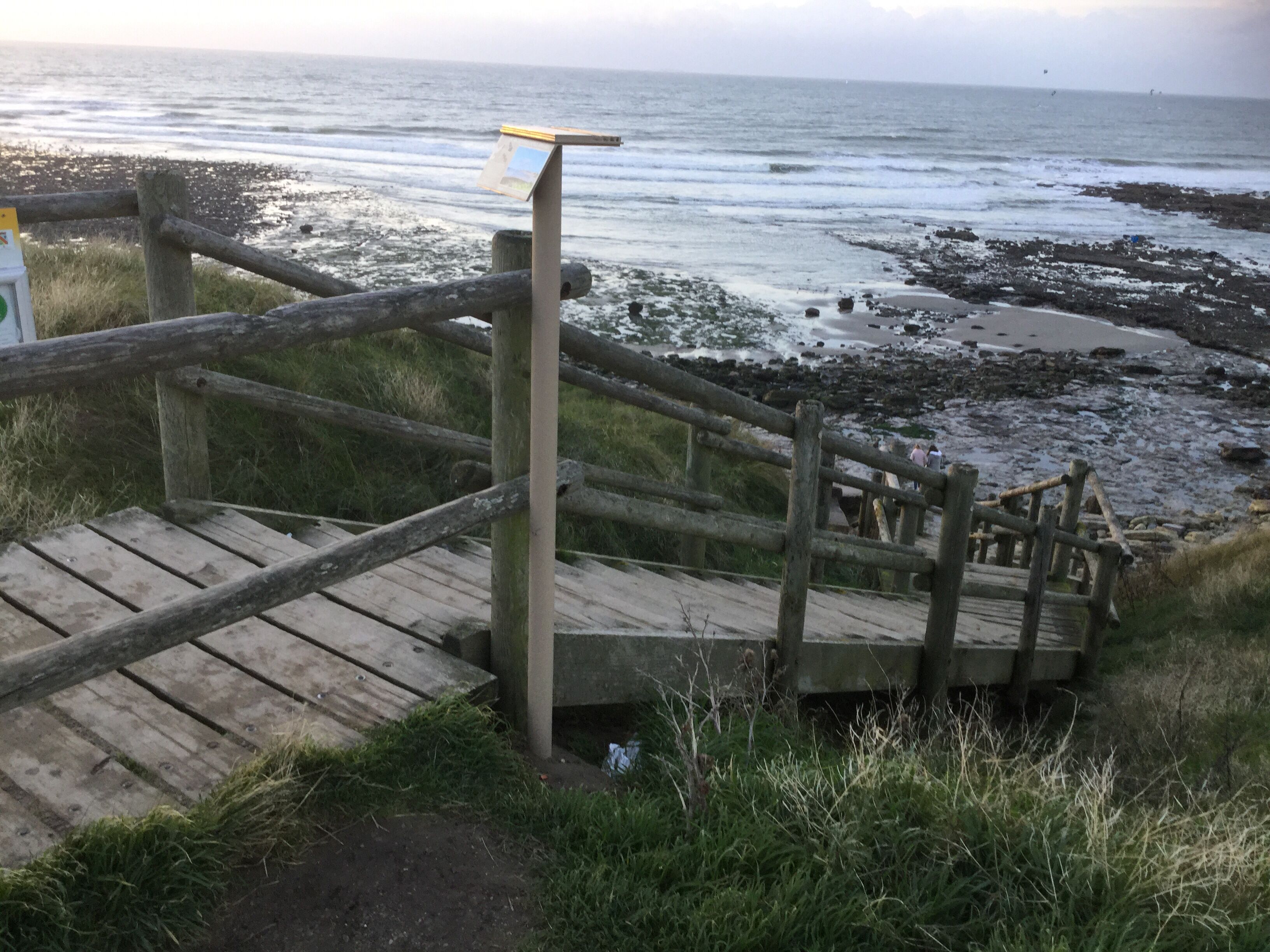 Una escalera de madera que desciende hacia una playa rocosa.