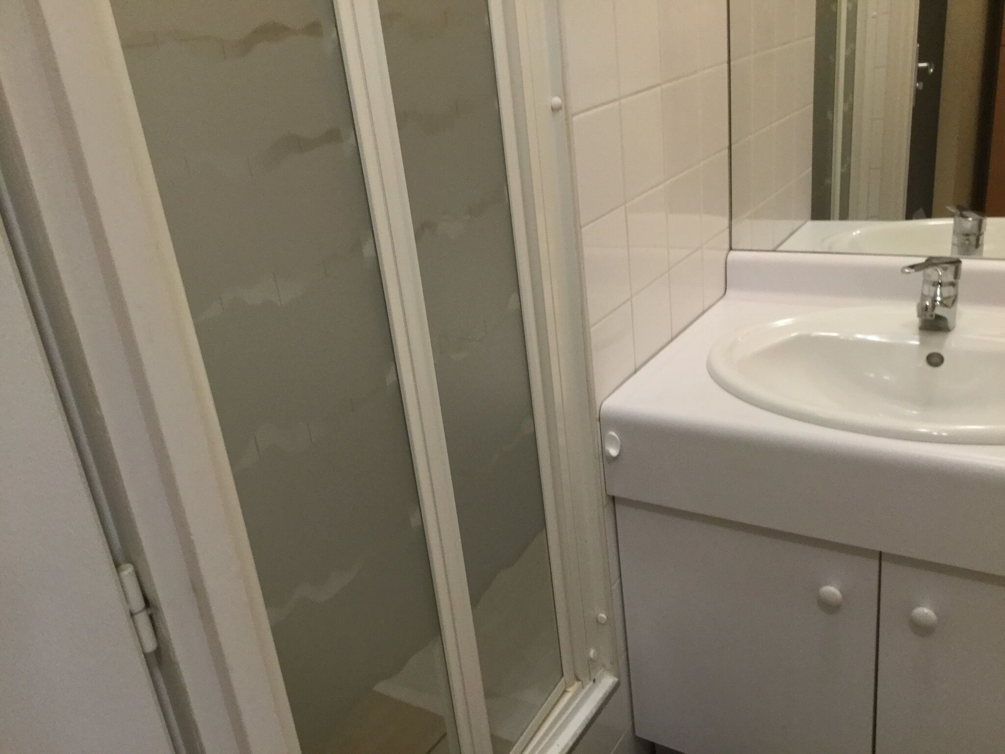 Une salle de bain avec un lavabo blanc, un miroir et une douche en verre.