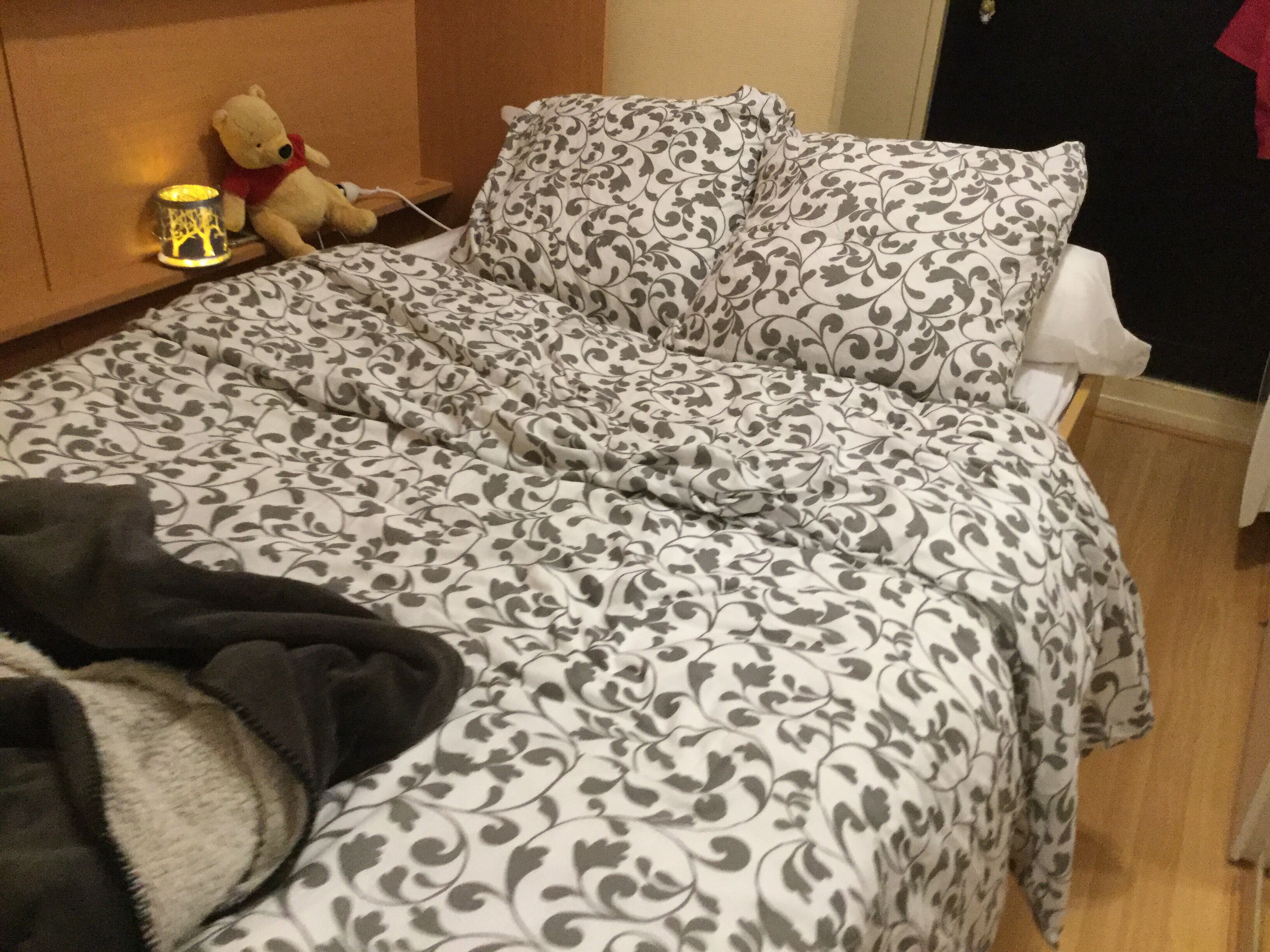 Un lit avec une couvre-lit à motifs, un ours en peluche et une lampe de chevet.