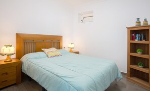 A bedroom with a bed, two bedside tables with lamps, a wooden headboard, a wall clock, and a bookshelf with books and a small plant. - Nice and comfortable Casa Avenida del Agujero, right on the beach (El Agujero)