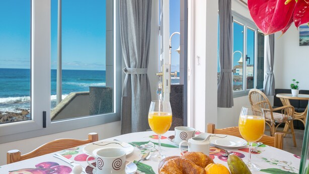 Een ontbijttafel met croissants, fruit en sinaasappelsap, met uitzicht op de oceaan.