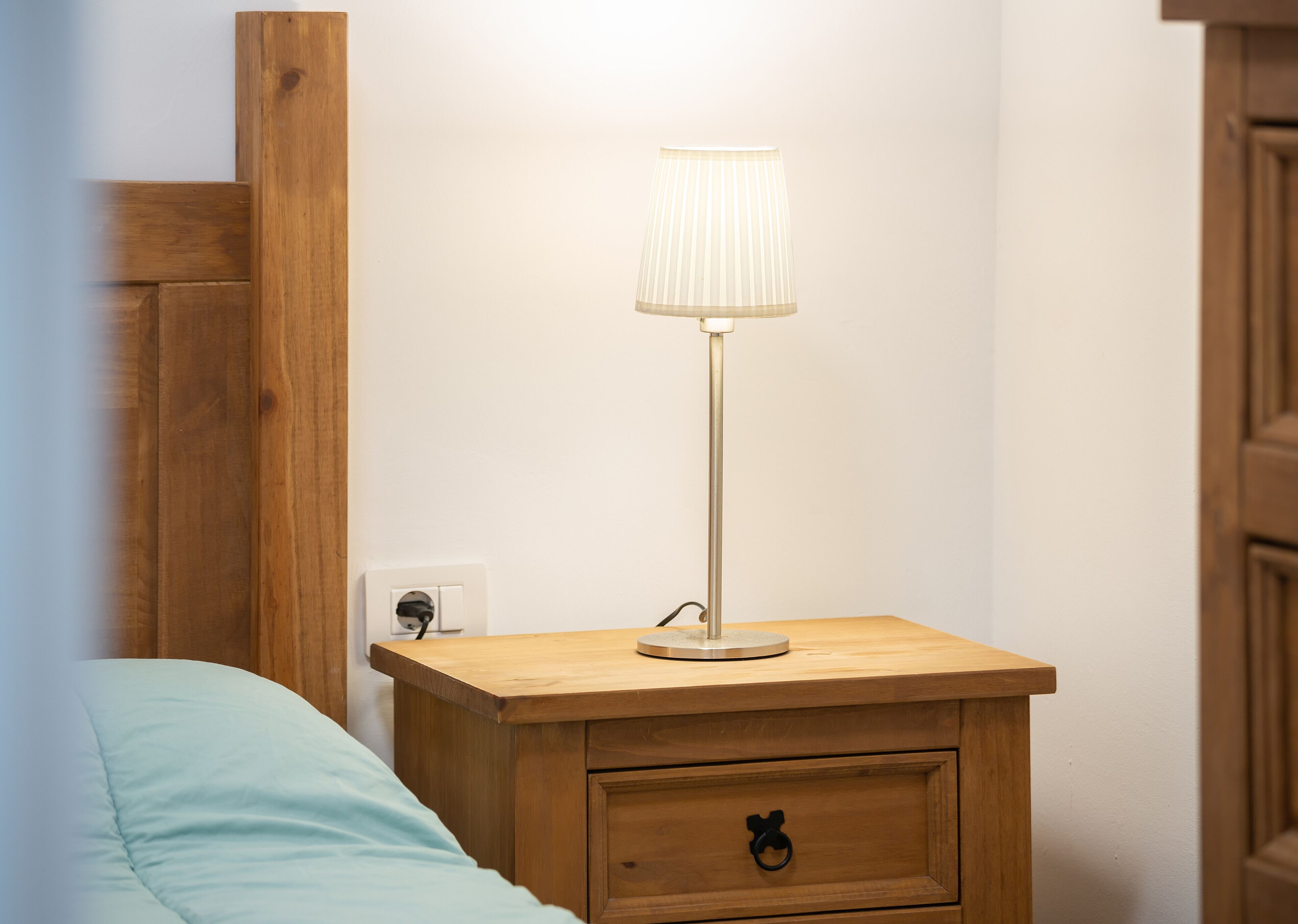 A wooden bedside table with a lamp, a power outlet, and a drawer with a Mickey Mouse handle.