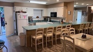 Una cocina compacta con armarios blancos, una isla central con sillas y una mesa de comedor.