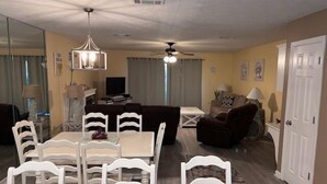 Un comedor con una mesa y sillas blancas, un ventilador de techo y un televisor al fondo.