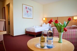 A hotel room with a bed, a round table with two bottles, a vase with red tulips, and a framed picture on the wall. - Double room standard - Hotel Am Jungfernstieg (Stralsund)
