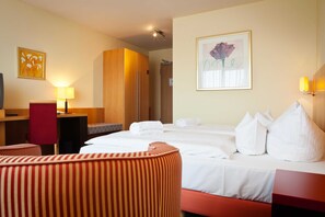 A hotel room with a bed, a desk, a chair, a sofa, a refrigerator, and a painting on the wall. - Double room standard - Hotel Am Jungfernstieg (Stralsund)