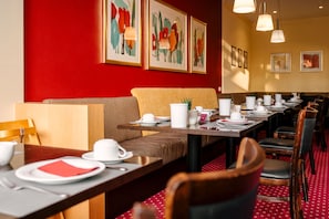 A restaurant with a red wall, multiple tables set with white tableware, and framed artwork above the seating area. - Double room standard - Hotel Am Jungfernstieg (Stralsund)
