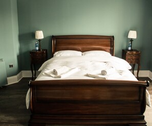 A neatly made bed with white linens in a room with teal walls and wooden headboard. There are two bedside tables with lamps on either side of the bed. - James Joyce guesthouse (Dublin)