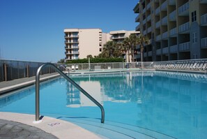 A swimming pool with a metal railing, surrounded by a fence, and buildings in the background.