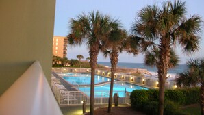 A pool area with palm trees, a view of the ocean, and a building in the background.