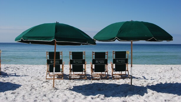Three beach chairs with green umbrellas labeled "WATER'S EDGE" on a sandy beach with the ocean in the background.