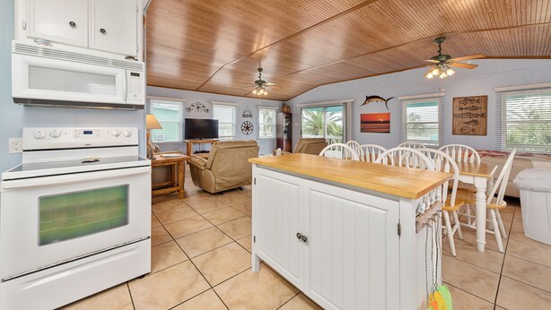 Een keuken met witte kasten, een houten plafond en een eethoek met witte stoelen en een houten tafel.