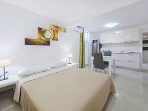 Habitación de hotel con cama, mesita de noche, lámpara, escritorio, silla y kitchenette.