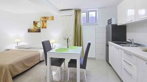 Quarto de hotel compacto com cama, mesa de jantar com cadeiras, cozinha compacta e televisão.