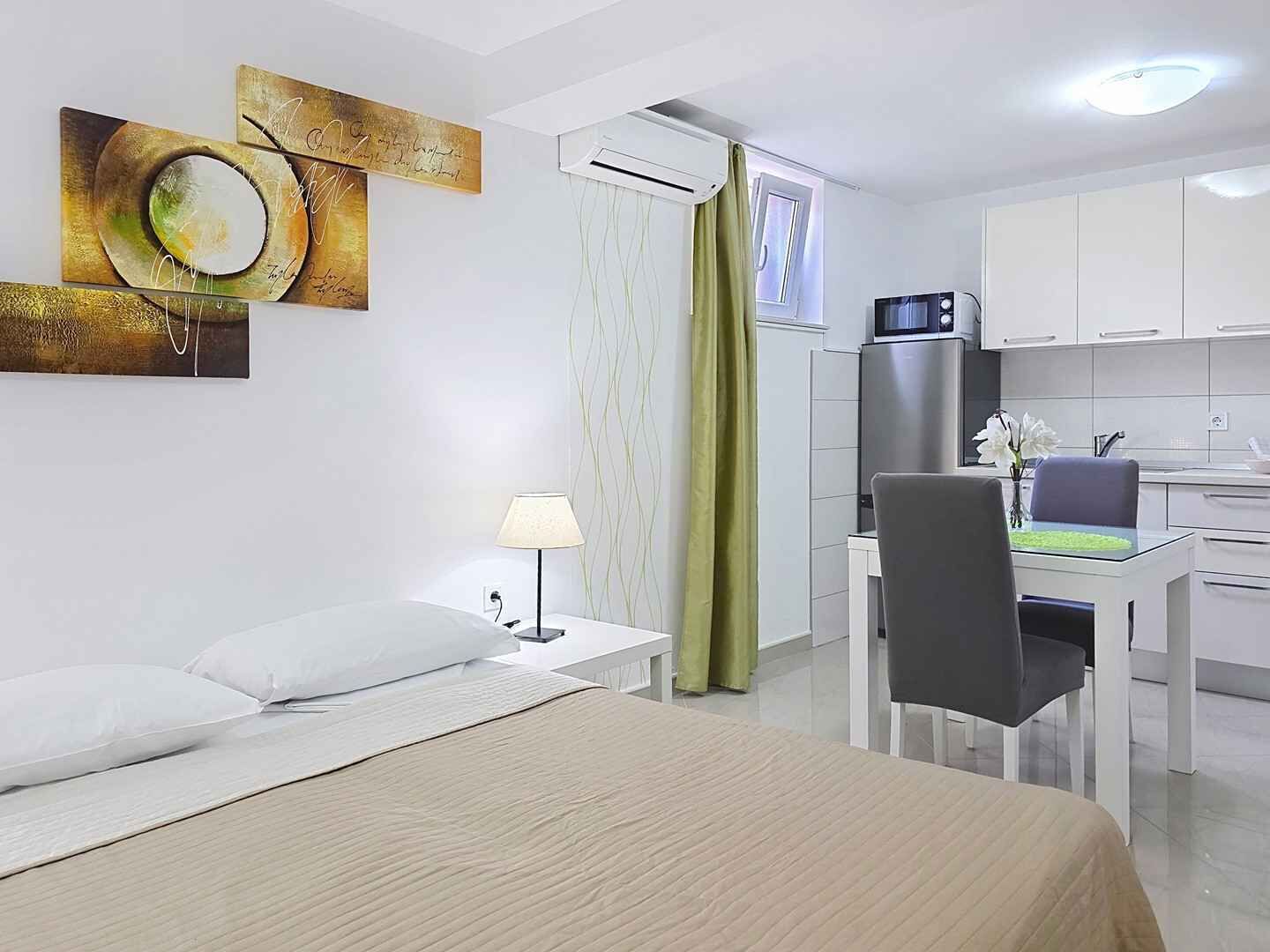 Een hotelkamer met een bed, een bureau, een stoel, een lamp, een airconditioner en een kitchenette.