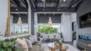 A modern living room with a sofa, dining table, and chairs, a large mirror, and a TV. - Designer Penthouse - Downtown Waterfront! (Kelowna)