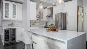 A modern kitchen with white cabinetry, stainless steel appliances, and a central island with bar stools. - Designer Penthouse - Downtown Waterfront! (Kelowna)