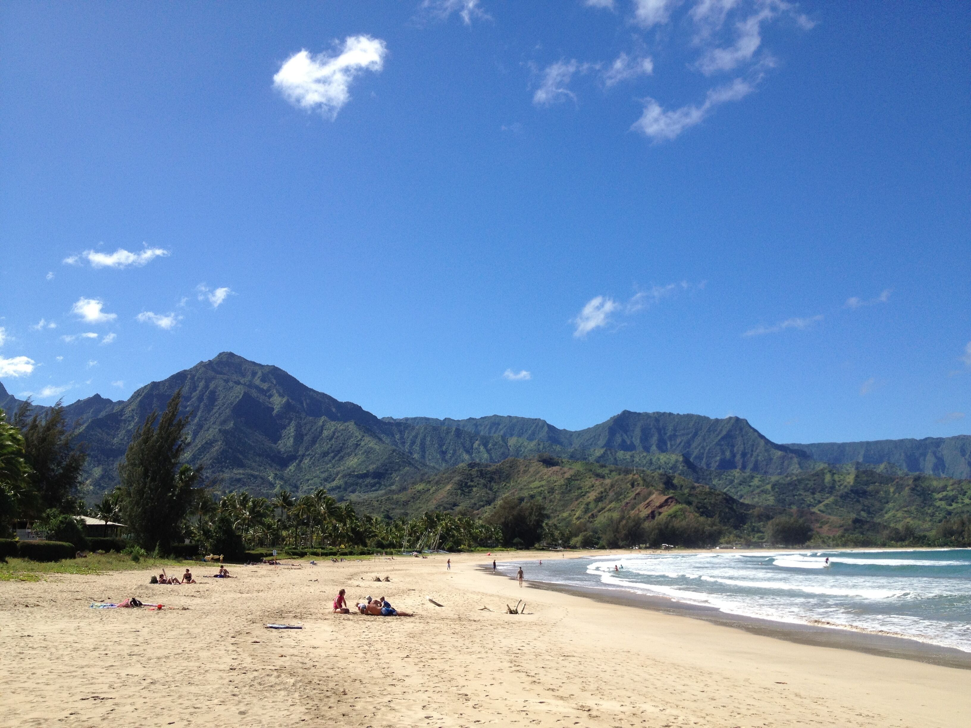 A beach with mountains in the background, sandy shore, and people relaxing.