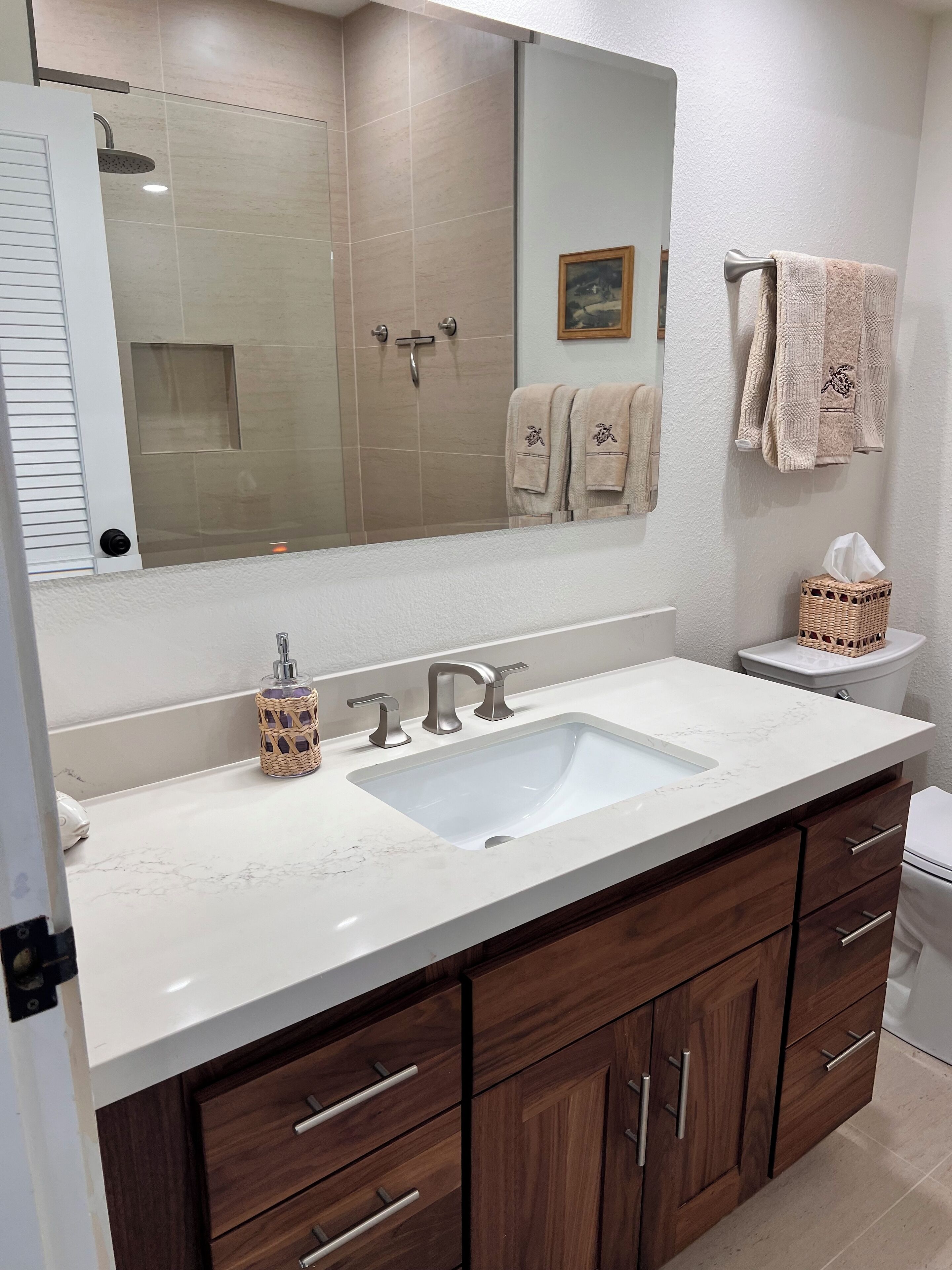 A bathroom with a white sink, wooden cabinets, a large mirror, and a toilet.