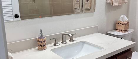 A bathroom with a white sink, wooden cabinets, a large mirror, and a toilet.
