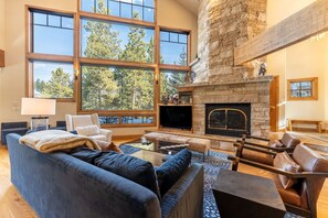 A spacious living room with a stone fireplace, large windows, and a cozy seating area. - Spacious Decks with Private Hot Tub Near Nordic Center and Golf Course! (Keystone)