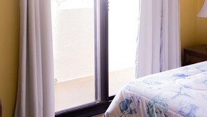 Un dormitorio con cama, ventana con cortinas y vista a un balcón.