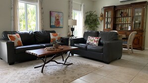 A living room with two black leather sofas, a wooden coffee table, a patterned rug, a potted plant, and a wooden cabinet with glass doors. - "Private Pool Oasis • 3-Min
Walk to Crystal Beach •
Tropical Escape" (Crystal Beach)