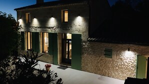 Un edificio de piedra con contraventanas verdes y una entrada iluminada al anochecer.