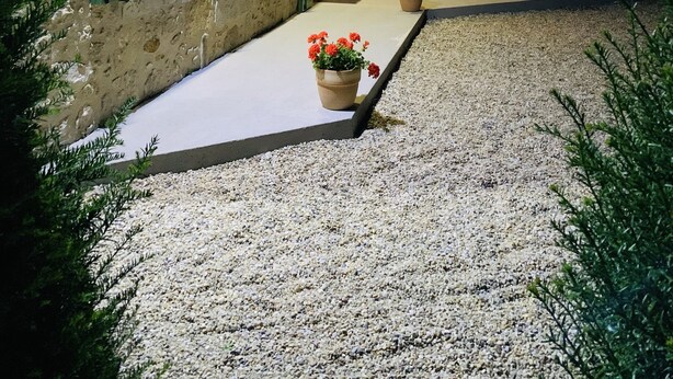 Un edificio de piedra con contraventanas verdes, un camino de grava y macetas con plantas.