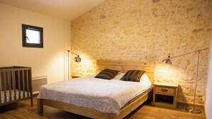 Un dormitorio con una cama de madera, dos mesitas de noche con lámparas, una cuna y una pared de piedra.