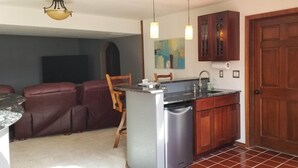 Cocina compacta con lavavajillas, armarios de madera y zona de comedor con sillas de cuero.