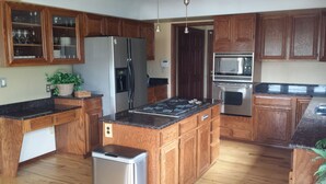 Una cocina con armarios de madera, un refrigerador de acero inoxidable, horno empotrado, microondas y encimera de granito.