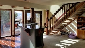 Amplia sala de estar con un gran ventanal que da a un patio exterior, una escalera de madera y una estantería empotrada.