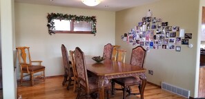 Comedor con mesa y sillas de madera, una ventana adornada con un adorno navideño y una pared decorada con fotografías.