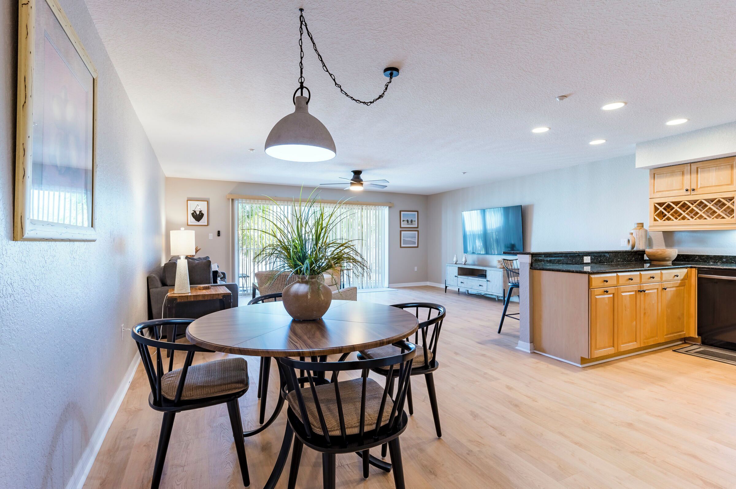 A modern kitchen with wooden cabinets, a dining area with a round table and chairs, and a ceiling fan.