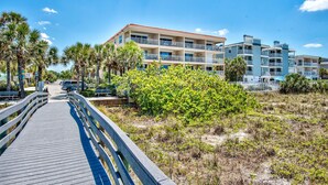 A wooden boardwalk leading to a beachfront hotel with multiple balconies and a clear blue sky. - Spacious, Luxury, Beach Condo with Pool (Indian Rocks Beach)