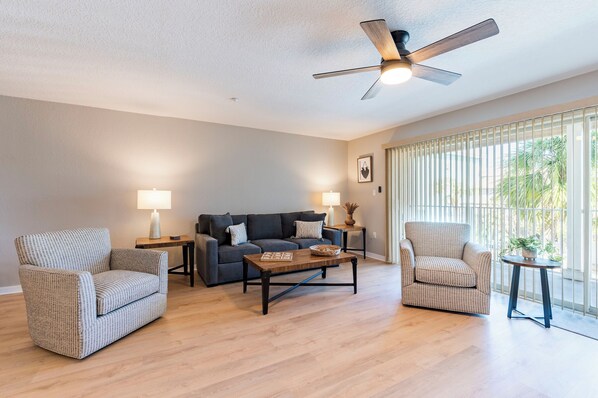 Ein Wohnzimmer mit Sofa, zwei Sesseln, einem Couchtisch und einem Deckenventilator.