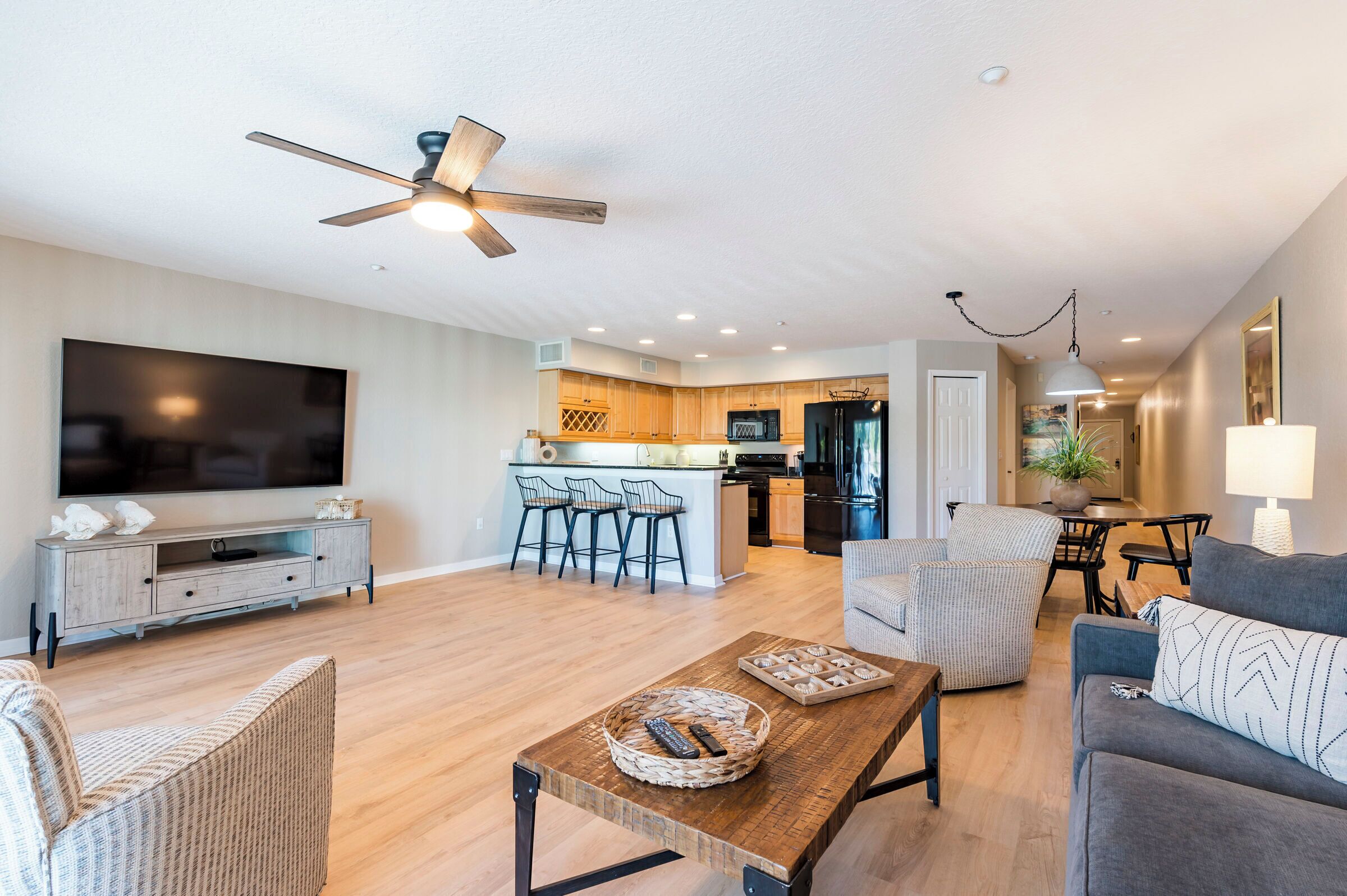 A modern living room with a TV, sofa, and coffee table, connected to a kitchen with bar stools.