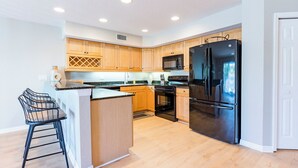 A modern kitchen with wooden cabinets, a black refrigerator, a microwave, and a stove. - Spacious, Luxury, Beach Condo with Pool (Indian Rocks Beach)