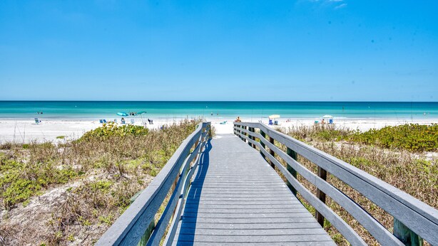 A wooden boardwalk leading to a beach with clear blue water and a few people in the distance. - Spacious, Luxury, Beach Condo with Pool (Indian Rocks Beach)