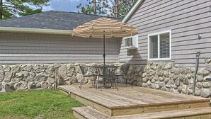 Un patio con terraza de madera, pared de piedra y una mesa con sillas bajo un paraguas a rayas.