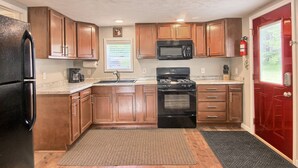 Una cocina compacta con armarios de madera, un refrigerador negro, un microondas y un horno.