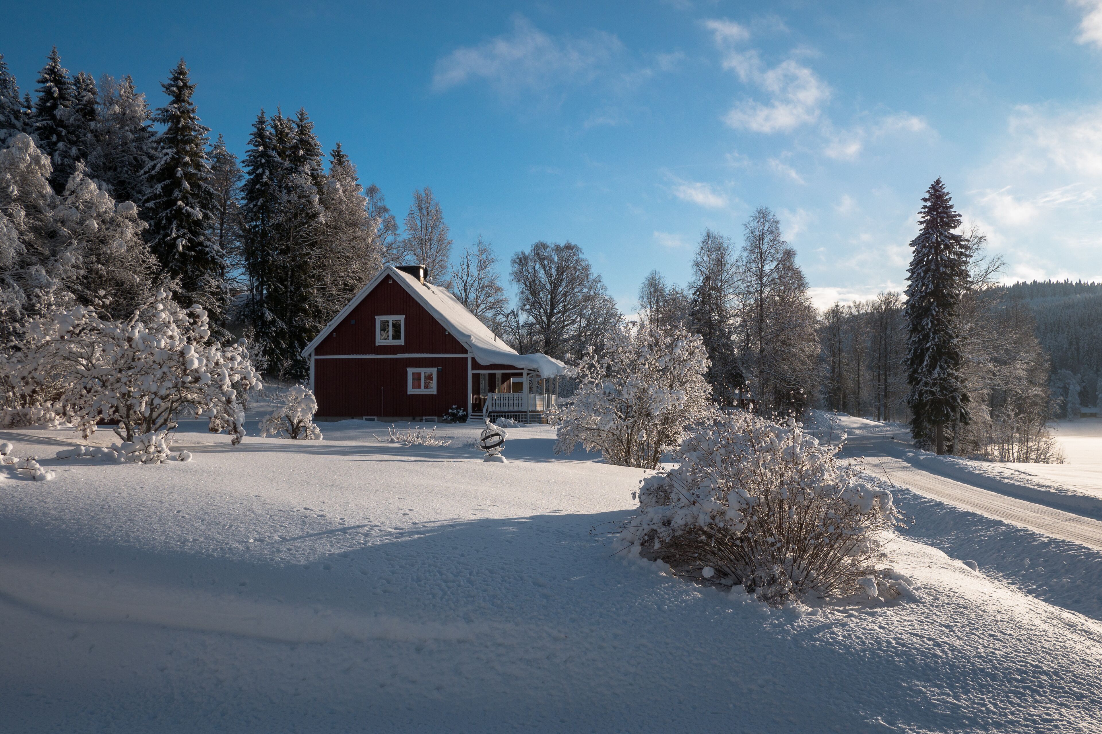 A red barn with a white porch, surrounded by snow-covered trees and a clear blue sky.