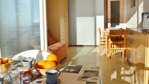 Une pièce bien éclairée, avec une table à manger dressée pour le petit-déjeuner, un canapé et un coin cuisine.