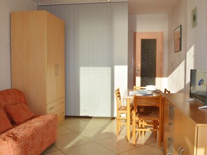 Et værelse med sofa, spisebord med stole, fjernsyn og et garderobeskab.