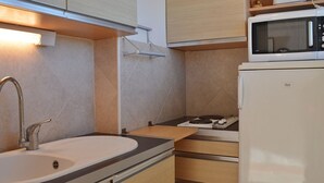 Une cuisine compacte équipée d’un évier, d’un four à micro-ondes, d’une cuisinière et de meubles de rangement en bois.