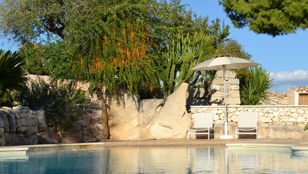 A swimming pool with a stone wall, two white chairs, and an umbrella. - MAESTRALE 1 bedroom apt 2/4 sleeps  with Pool - Modica - Sicily (MODICA)
