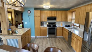 A kitchen with wooden cabinets, stainless steel appliances, and a dining area with a table and chairs. - Steps to Lake Erie near Lakeside - Private Hot Tub, Seasonal Pool, Recreation (Lakeside Marblehead)