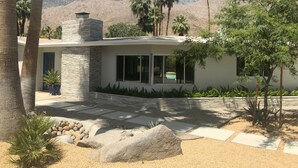 A modern house with a stone facade, large windows, and a landscaped garden with palm trees and a rock feature.